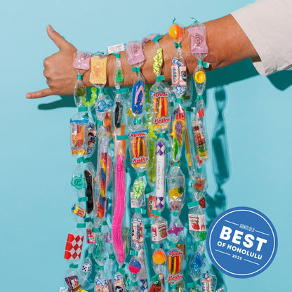 Person displaying colorful Trinket Lei on their arm with various small items on a blue background, with 'Best of Honolulu' badge.